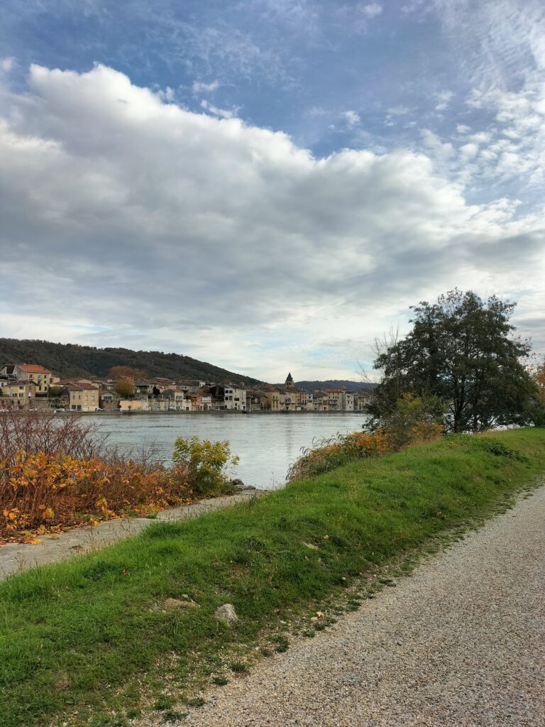Sentier de la Via Rhôna longeant le Rhône avec vue sur un village